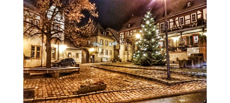 Marktplatz mit Kopfsteinpflaster, Fachwerkäusern und Weihnachtsbaum mit brennenden Lichtern