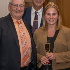 Kiedricher Weinkönigin Julia, mit goldenem Diadem auf den blonden langen Haaren und einem beigem Blazer und einem schwarzem Shirt und einer schwarzen Hose, in der Mitte Bürgermeister Winfried Steinmacher mit blauem Sakko, weißem Hemd, Kravatte und Brille und links davon der Erste Beigeordnete Rüdiger Wolf, mit schwarzem Sakko und orangenem Hemd mit gestreifter Kravatte und Brille.