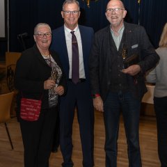 Bürgermeister Steinmacher (Mitte) mit dem Wallufer Bürgermeister a.D. Manfred Kohl (rechts) und seiner Ehefrau (links) stehen, alle im dunklen Anzug und mit Brille, vor goldenen Zahlenballons, die 2025 zeigen, vor einem blauem Vorhang.