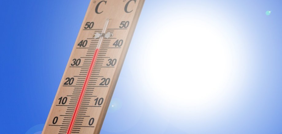 Ein Termometer aus Holz, bei dem eine Temperatur von 39 Celcius angezeigt wird vor einem blauem Himmel mit strahlender Sonne.