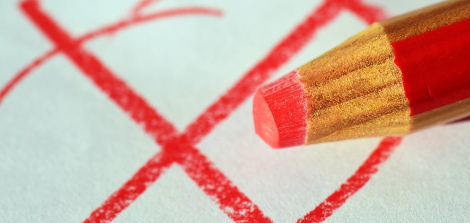 Auf einem weißen Zettel wurde ein rotes Kreuz mit einem Kreis dumrum gemalt. Man sieht den dicken rot beige gestreiften Buntstift mit roter Mine. 