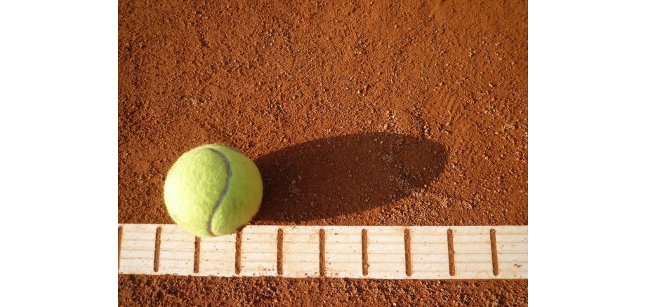 Gelber Tennisball auf roten Boden des Tennisspielfeldes und einer weißen gestreiften Linie.