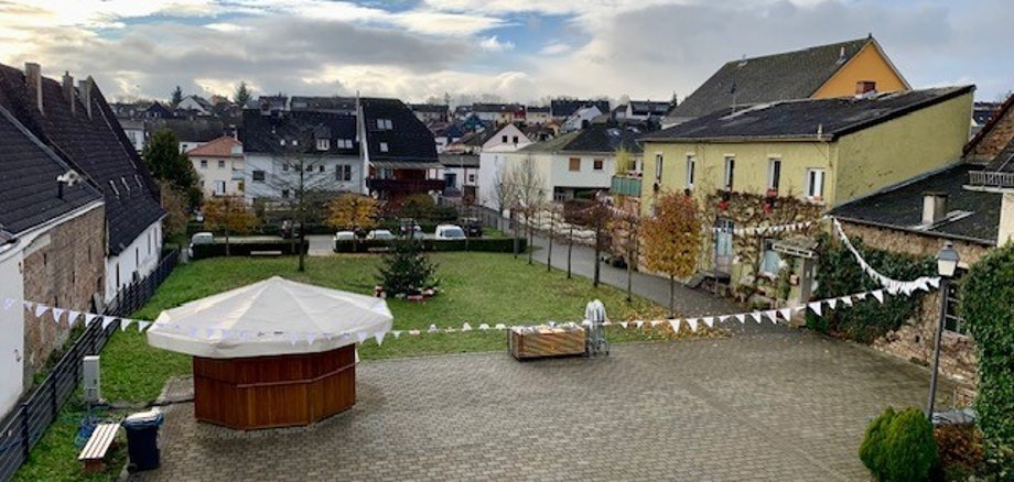 Blick auf den Josef-Staab-Platz mit aufgebautem Glühweinstand und geschmücktem Tannenbaum und einer weißen Wimpelkette auf der Bilder gemalt sind.