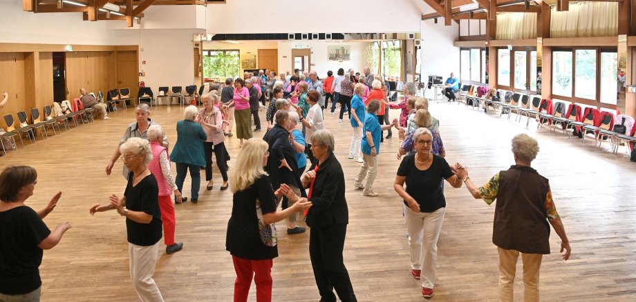 Senioren, die miteinander in einem großem Saal tanzen.