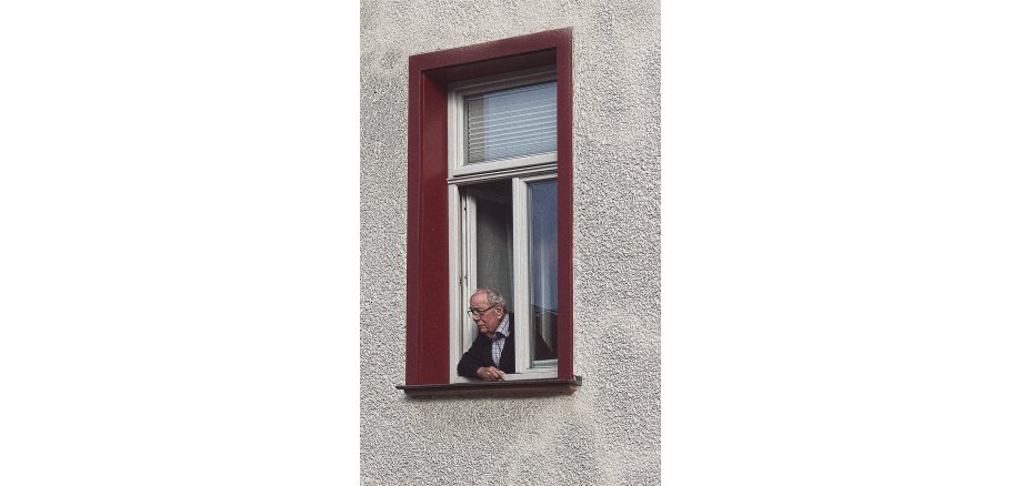 Alter Mann mit Brille schaut aus einem geöffnetem Fenster.