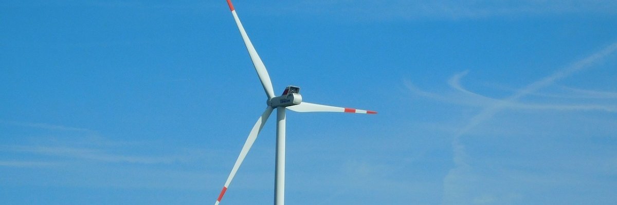 Vor einem blauen Himmel, ist der obere Teil eines weißen Windrates mit roten Streifen zu sehen.